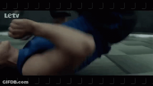 A Man Is Laying On The Floor While Another Man Is Running In A Hallway . GIF