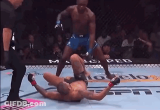 A Man Is Laying On The Ground In A Boxing Ring While A Referee Watches . GIF