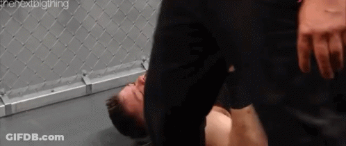 A Man Is Laying On The Ground In A Boxing Ring While Another Man Is Standing Over Him . GIF