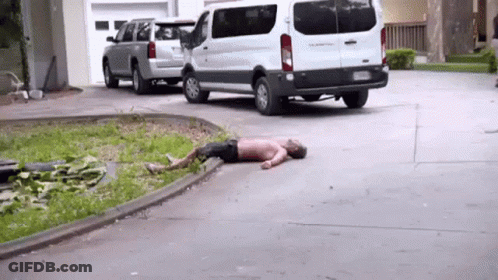 A Man Is Laying On The Ground In A Driveway Next To A White Van . GIF