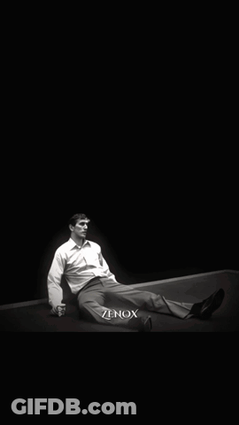 A Man Is Laying On The Ground In Front Of A Large Portrait Of A Man With A Beard And The Word Zenox Below Him GIF