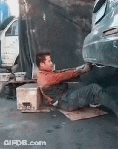 A Man Is Laying On The Ground Working On A Car 'S Exhaust Pipe . GIF