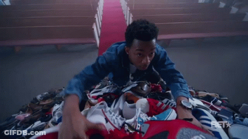 A Man Is Laying On Top Of A Pile Of Shoes With A Bet Logo In The Background GIF