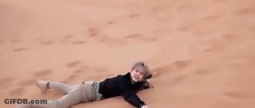 A Man Is Laying On Top Of A Sand Dune In The Desert . GIF