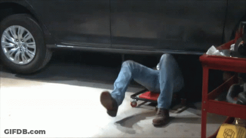 A Man Is Laying Under A Car In A Garage With His Head Underneath The Car GIF