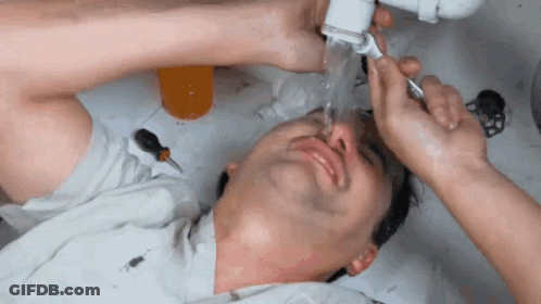 A Man Is Laying Under A Sink With Water Coming Out Of The Pipes GIF