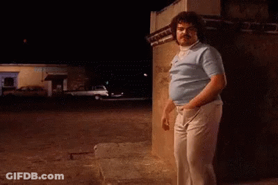 A Man Is Leaning Against A Wall In A Parking Lot At Night . GIF