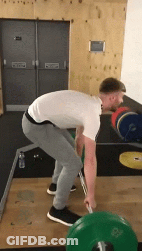 A Man Is Lifting A Barbell In A Gym . GIF