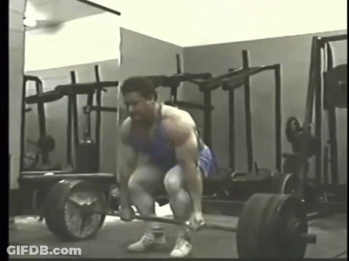 A Man Is Lifting A Barbell In A Gym In Front Of A Mirror . GIF