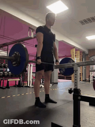 A Man Is Lifting A Barbell In A Gym With A Pink Wall Behind Him GIF