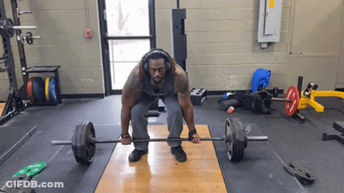 A Man Is Lifting A Barbell In A Gym With Headphones On GIF