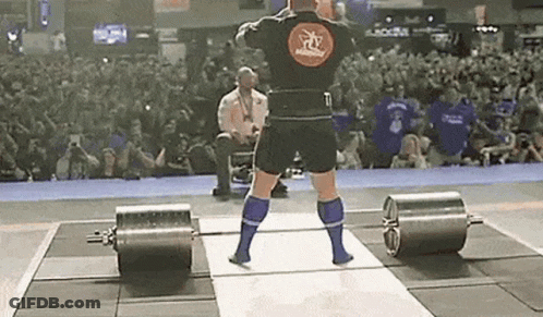 A Man Is Lifting A Barbell On A Stage In Front Of A Crowd Of People . GIF