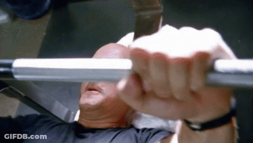 A Man Is Lifting A Barbell While Sitting On A Bench In A Gym . GIF