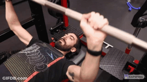A Man Is Lifting A Barbell While Wearing A Shirt That Says ' Kapwing ' On It GIF