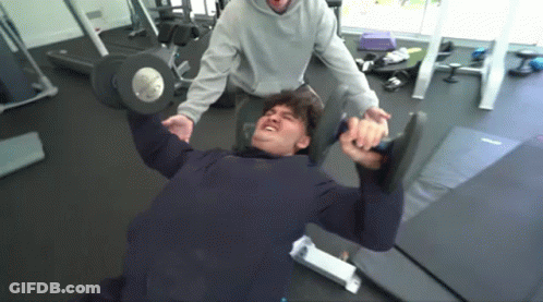 A Man Is Lifting A Dumbbell In A Gym . GIF
