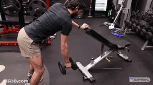 A Man Is Lifting A Dumbbell On A Bench In A Gym With A Caption That Says Kapwing GIF