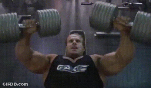 A Man Is Lifting Dumbbells In A Gym Wearing A Black Tank Top That Says Fake GIF