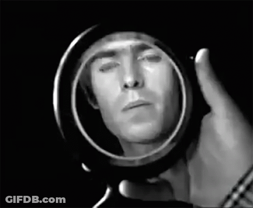 A Man Is Looking At His Face In A Mirror . GIF