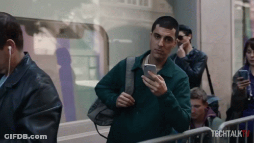 A Man Is Looking At His Phone In Front Of A Sign That Says Tech Talk Tv GIF