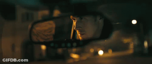 A Man Is Looking At His Reflection In The Rear View Mirror Of A Car . GIF