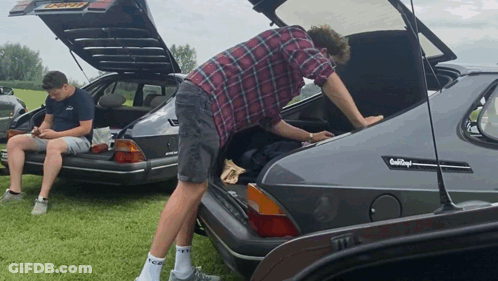 A Man Is Looking Into The Trunk Of A Car That Says Saab Royal GIF