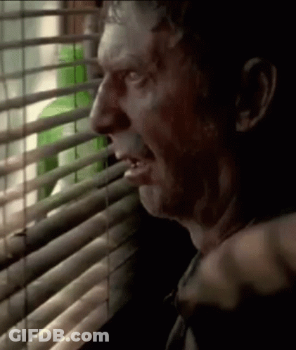 A Man Is Looking Out A Window With Blinds And A Green Bottle Behind Him . GIF