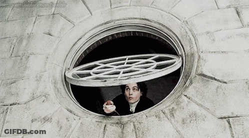 A Man Is Looking Out Of A Round Window With A Circular Grid On It GIF