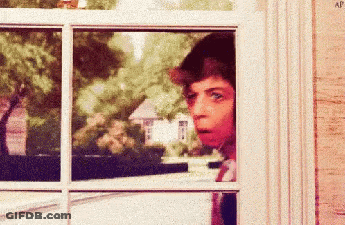 A Man Is Looking Out Of A Window And Making A Funny Face . GIF