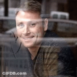 A Man Is Looking Out Of A Window And Smiling . GIF