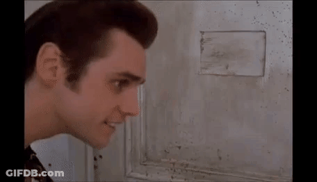 A Man Is Looking Through A Hole In A Wall At Something . GIF