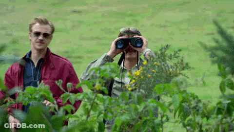 A Man Is Looking Through Binoculars In A Field While Another Man Looks On . GIF