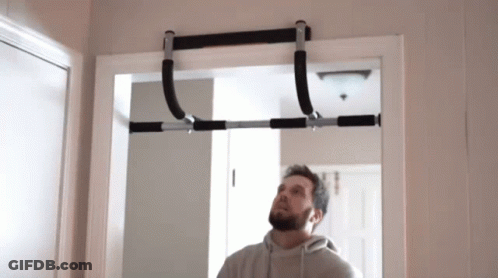 A Man Is Looking Up At A Pull Up Bar Hanging From A Doorway . GIF