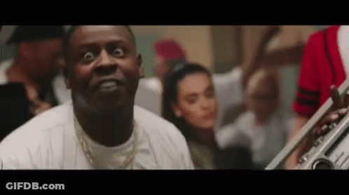A Man Is Making A Funny Face While Playing A Trumpet In Front Of A Crowd . GIF