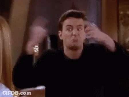 A Man Is Making A Funny Face While Sitting At A Table With His Arms Outstretched In A Room . GIF