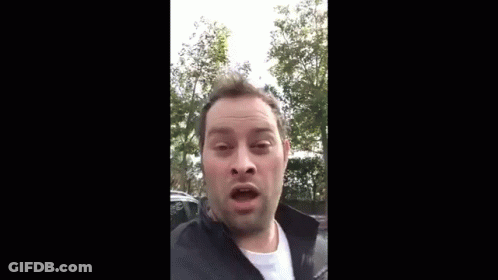 A Man Is Making A Funny Face While Wearing A Black Jacket And A White Shirt . GIF