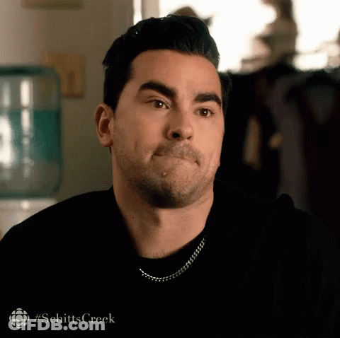 A Man Is Making A Funny Face While Wearing A Black Shirt And A Silver Chain . GIF