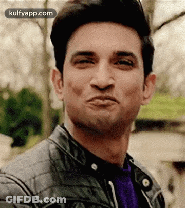 A Man Is Making A Funny Face While Wearing A Leather Jacket And A Purple Shirt . GIF
