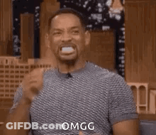 A Man Is Making A Funny Face With His Mouth Open And A Fist In His Hand . GIF
