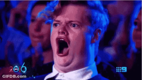A Man Is Making A Funny Face With His Mouth Open While Sitting In A Crowd Of People . GIF