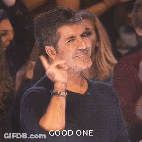 A Man Is Making A Peace Sign With His Hand While Sitting In A Crowd Of People . GIF