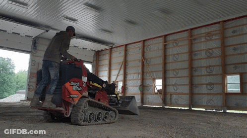 A Man Is Operating A Ditch Witch Tractor In A Garage GIF
