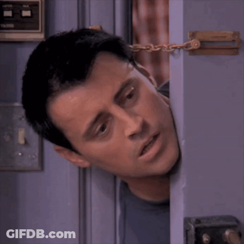 A Man Is Peeking Out From Behind A Door With A Chain Around His Neck GIF