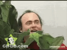 A Man Is Peeking Out From Behind A Plant With A Star On His Shirt GIF