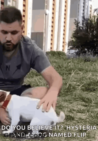 A Man Is Petting A Small White Dog In A Field . GIF