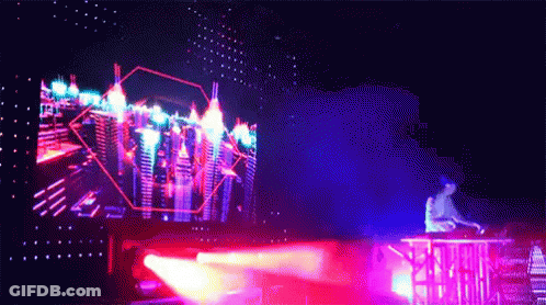 A Man Is Playing A Dj Set In Front Of A Large Screen With A City In The Background GIF