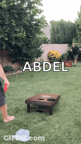 A Man Is Playing A Game Of Cornhole In A Backyard With The Name Abdel On The Bottom GIF