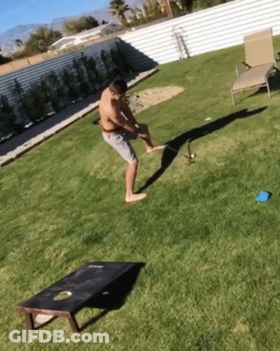 A Man Is Playing A Game Of Cornhole In The Backyard GIF