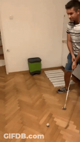 A Man Is Playing A Game Of Golf On A Hardwood Floor GIF