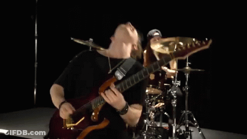 A Man Is Playing A Guitar And A Woman Is Playing Drums In A Band . GIF