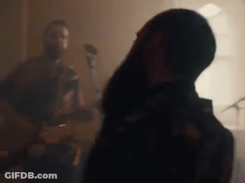 A Man Is Playing A Guitar And A Woman Is Singing Into A Microphone In A Room . GIF